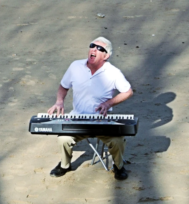 a man wearing sunglasses playing a keyboard in the sand