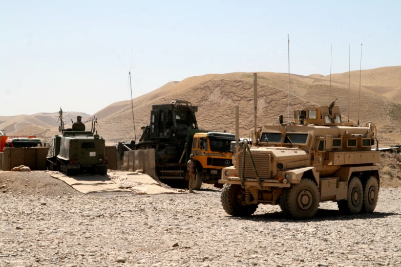 three army vehicles sitting in a dusty desert area