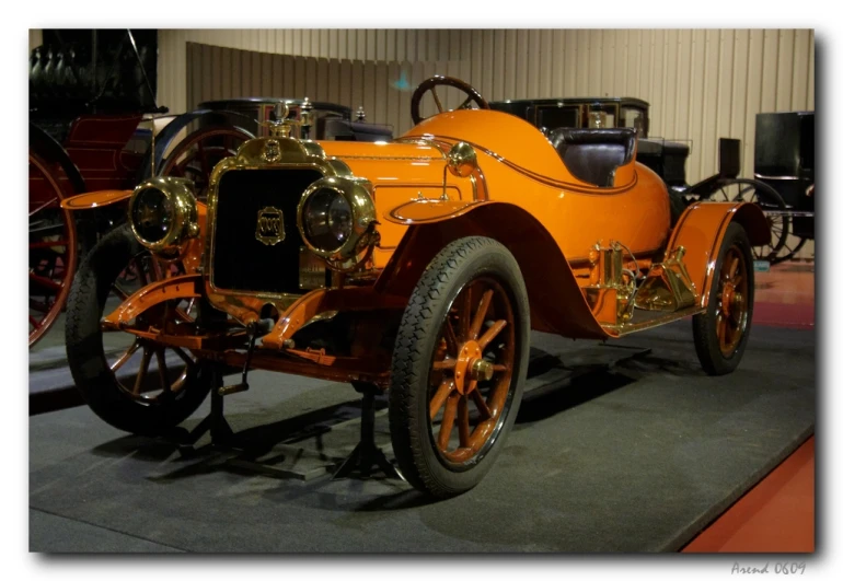 an antique orange car sits in front of a building