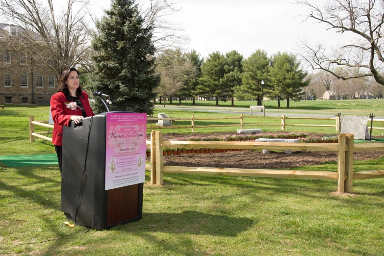 a woman stands at a podium in front of an open grassy field