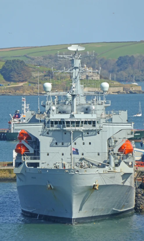 large navy boat docked at pier near a mountain