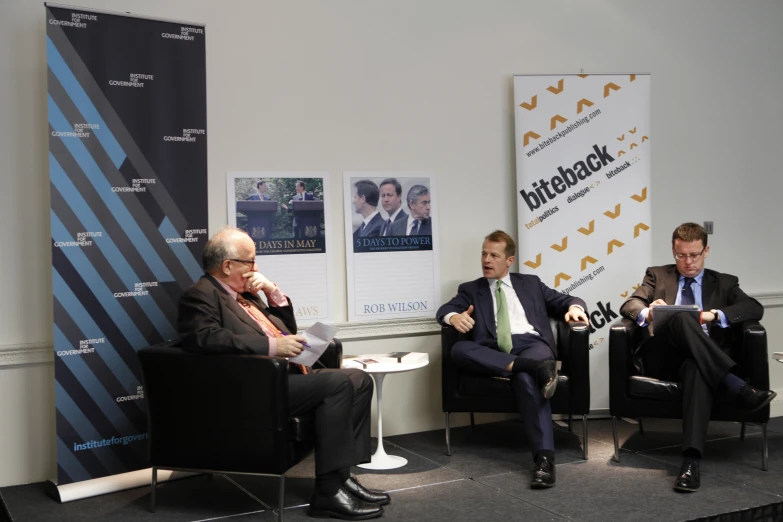 three men in suits are sitting in chairs