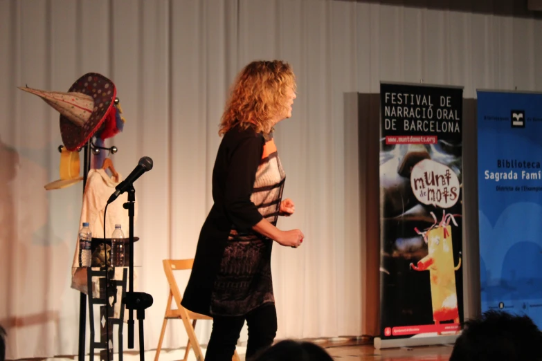 a lady standing next to a microphone in front of a curtain