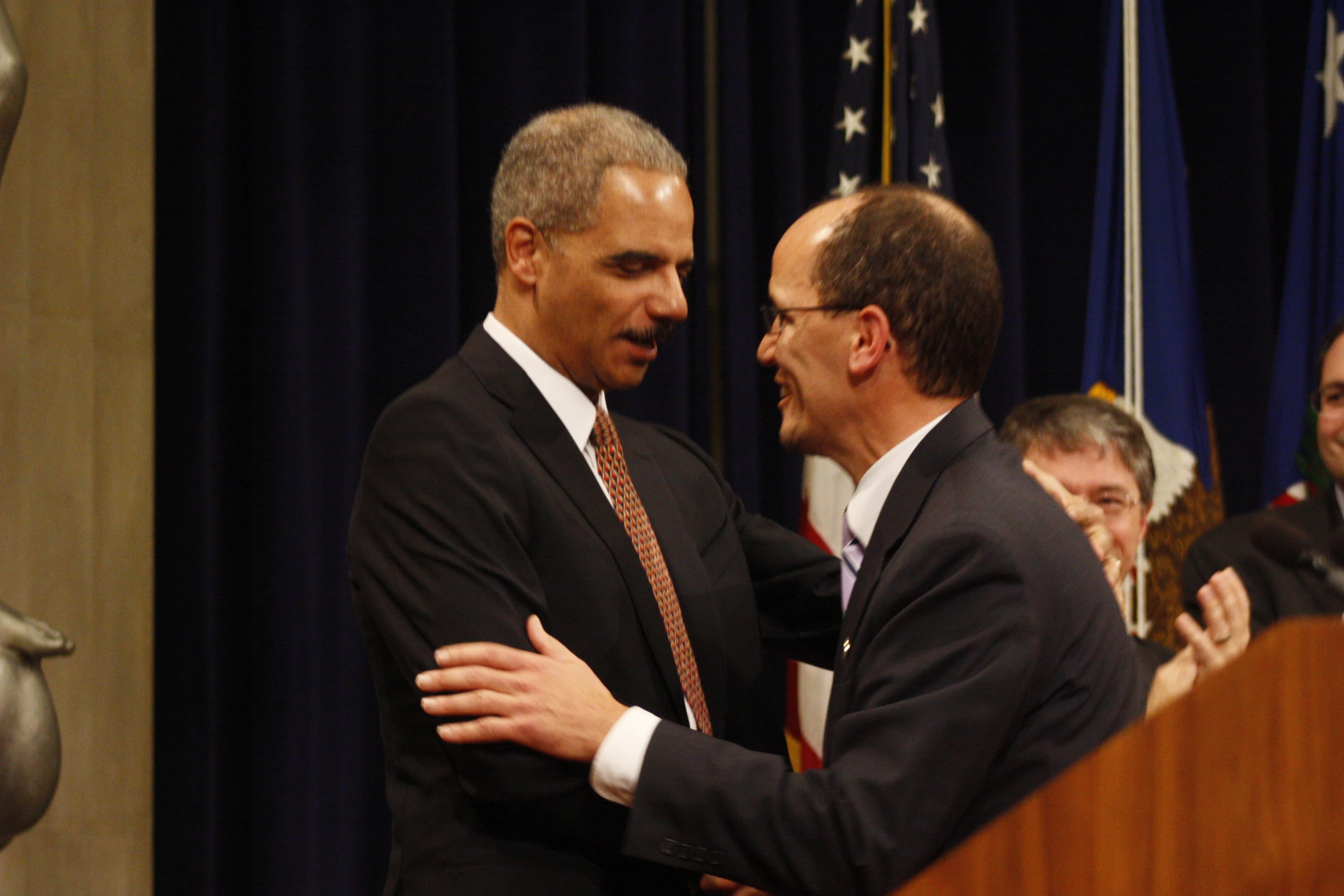 the president greets two men standing at a podium