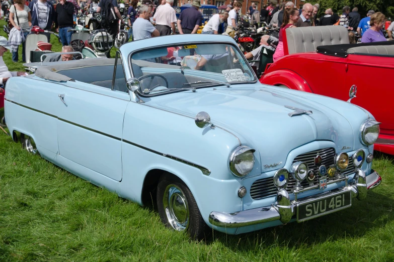 classic blue car parked in grass with people nearby