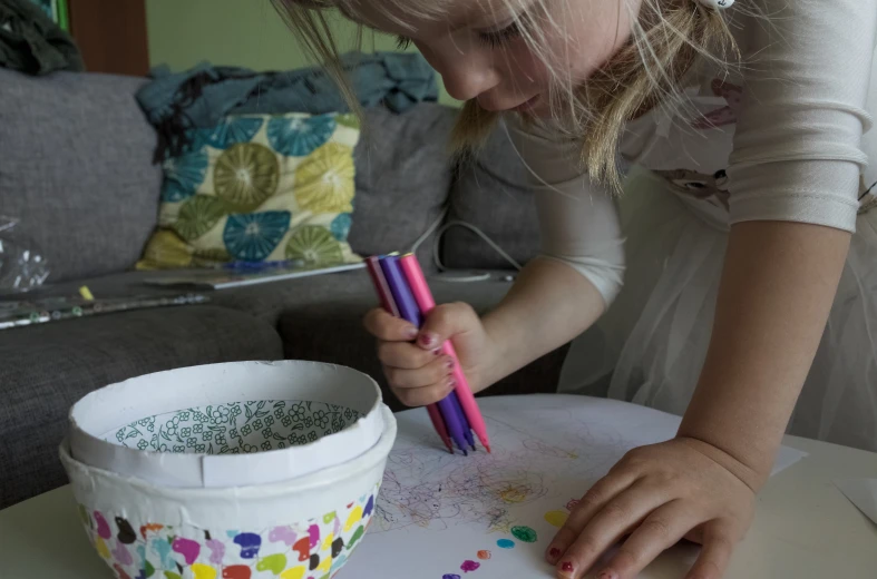 a girl sitting at a table with some colored pens