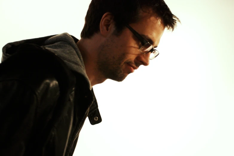 a man in a leather jacket, glasses and dark hair with a cell phone