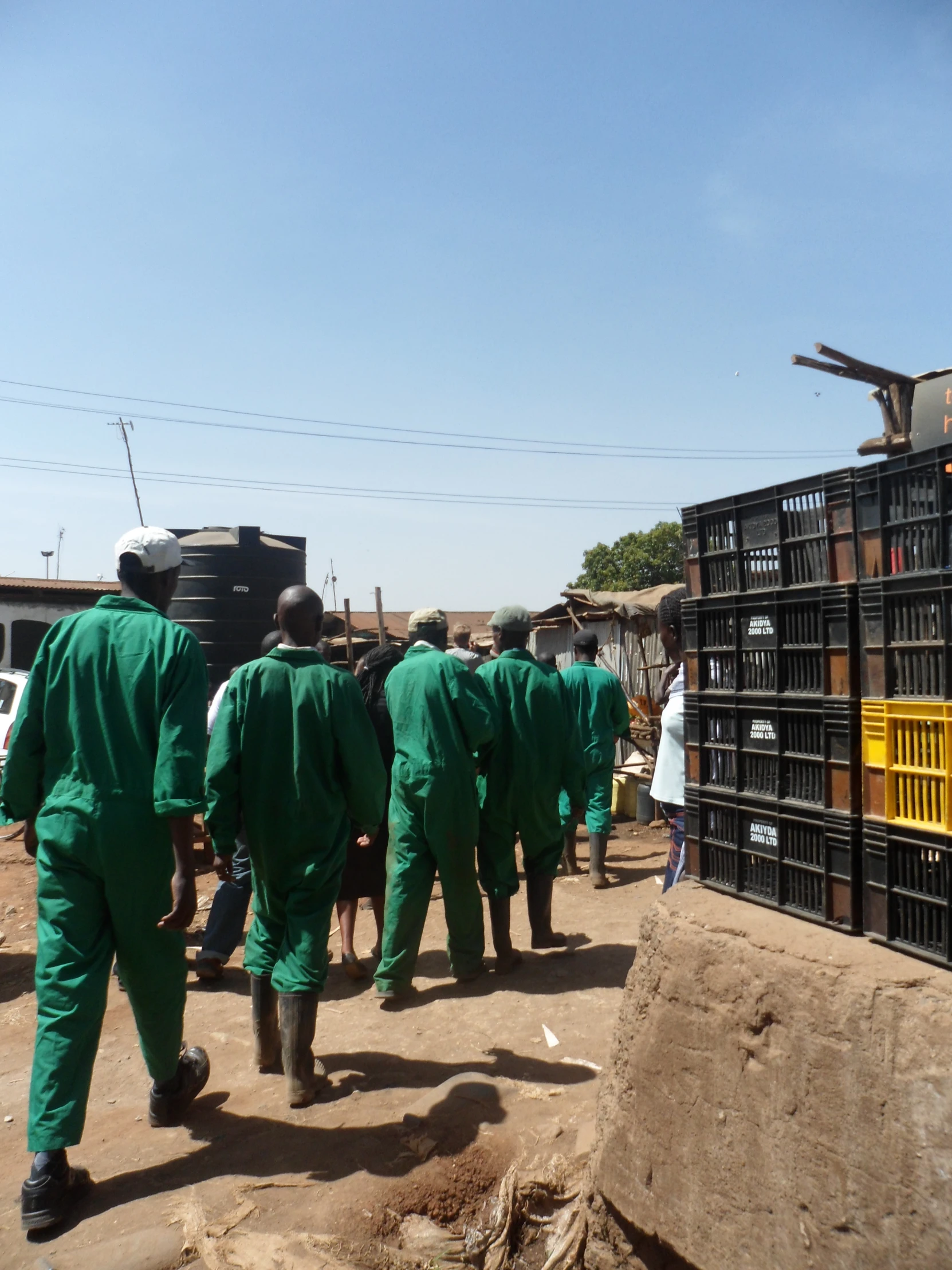 men are walking down the dirt road near many cages