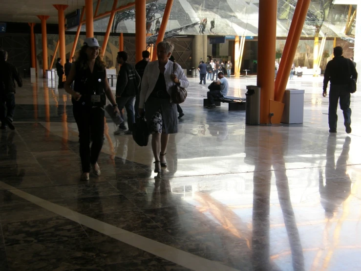 a group of people walking through a hallway next to tall orange pillars