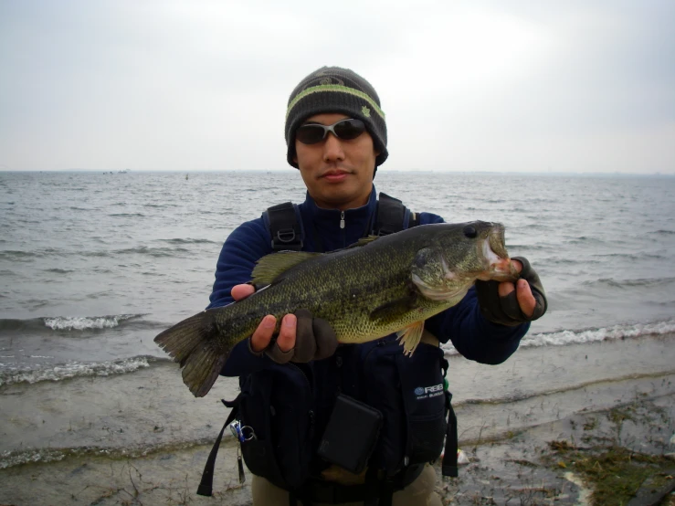 a man on a beach holding up a fish