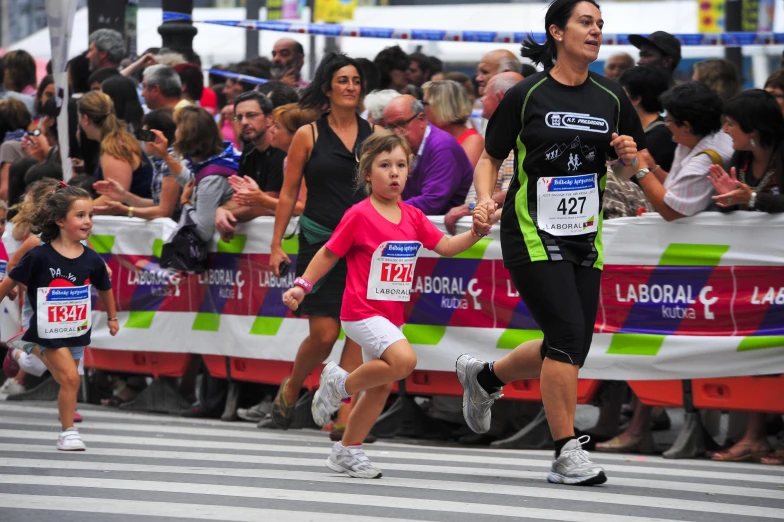 the girl in the running costume is holding a woman's hand and they are running through a marathon line of spectators