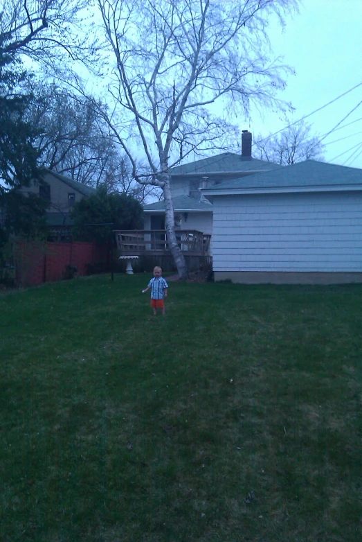 a little boy standing in the grass on a yard
