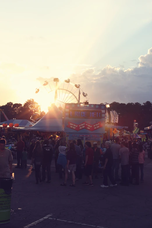 a crowd gathers at an outdoor fair with bright sunlight streaming through the sky