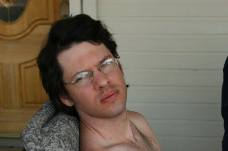a shirtless man wearing glasses is sitting outside