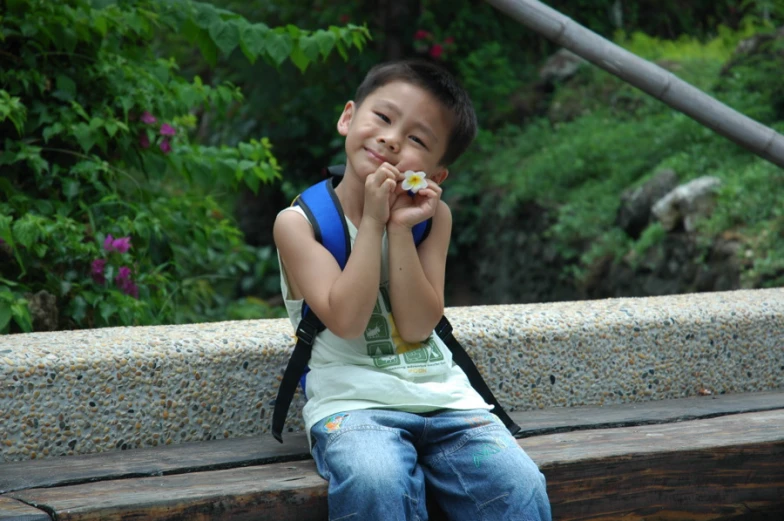 the little child is sitting on a bench in a park and holding flowers