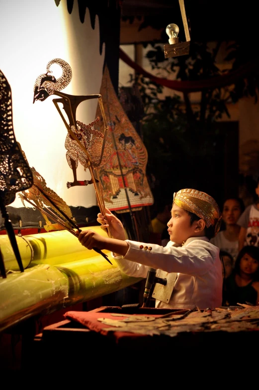 a small child wearing an oriental style headdress holding sticks