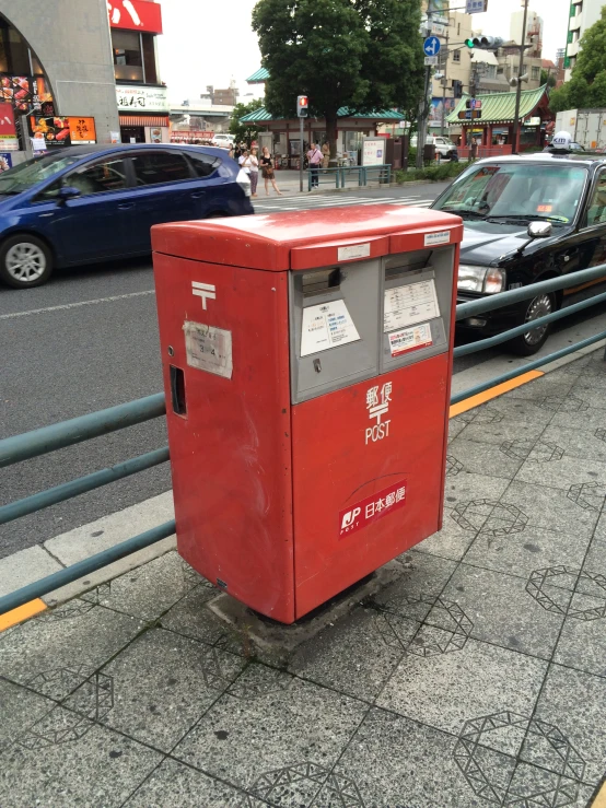 a red trash box is sitting on the side of the road