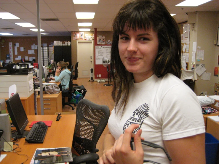 a woman holds up her electronic device in a room with many desks