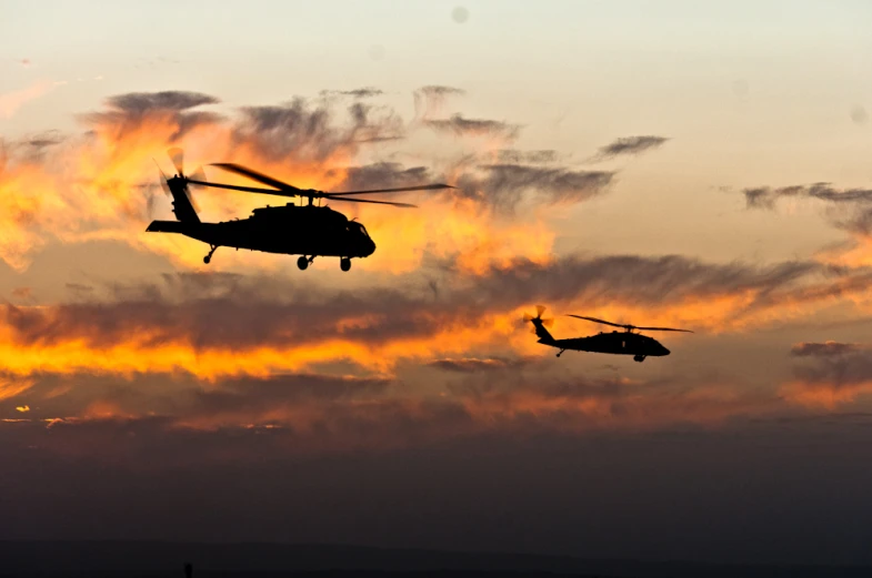 three helicopters are flying at sunset on a cloudy day