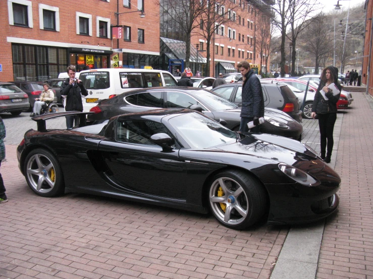 a man looks at a black sports car parked along a busy street