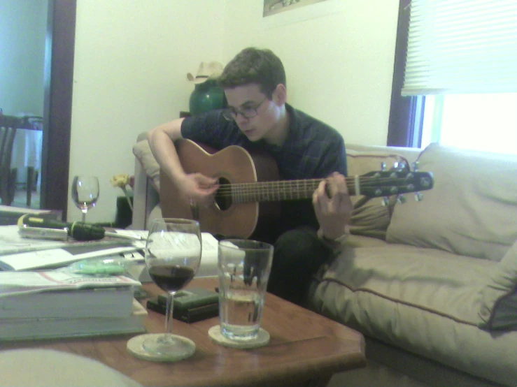 a young man plays guitar while drinking wine