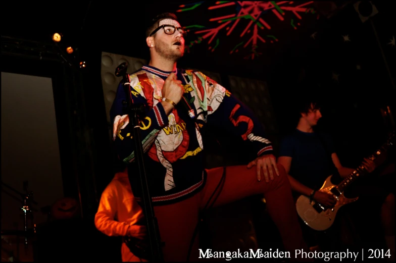 a man with glasses holding a guitar standing on stage