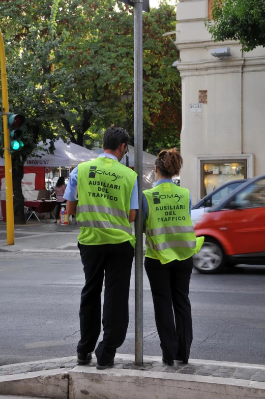 two people in neon vests walking past a traffic light