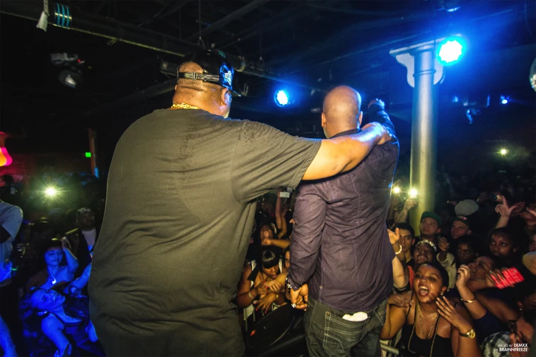 two men at a concert and one is holding his hands out