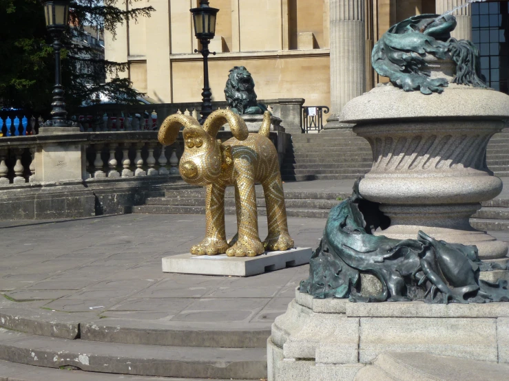 a gold colored sculpture of a dog holding a rose with another statue in the background