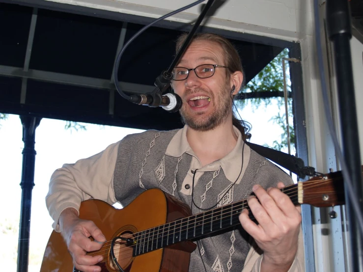 man singing while playing guitar on stage at outdoor venue