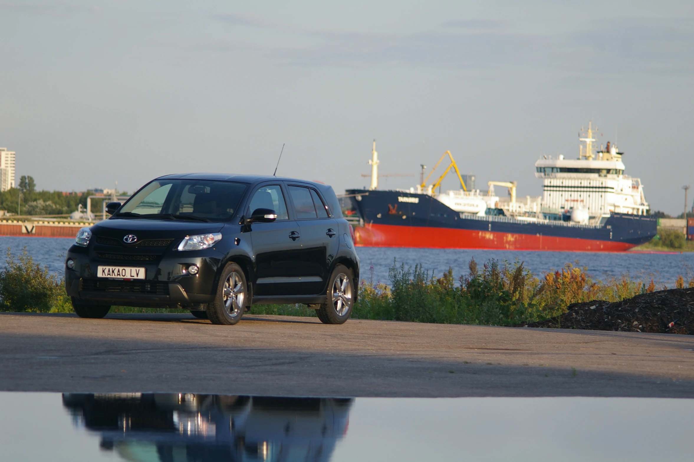 a suv parked on a shore with ships in the water