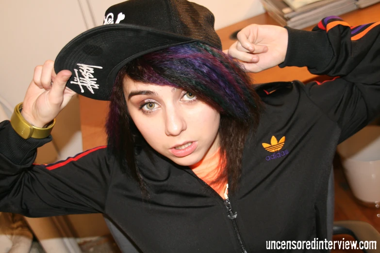 woman with dyed hair and a black hat in a bedroom