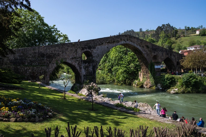 people walking by an old stone bridge near a river