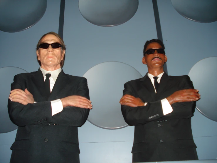 two men in black suits wearing sunglasses and standing side by side