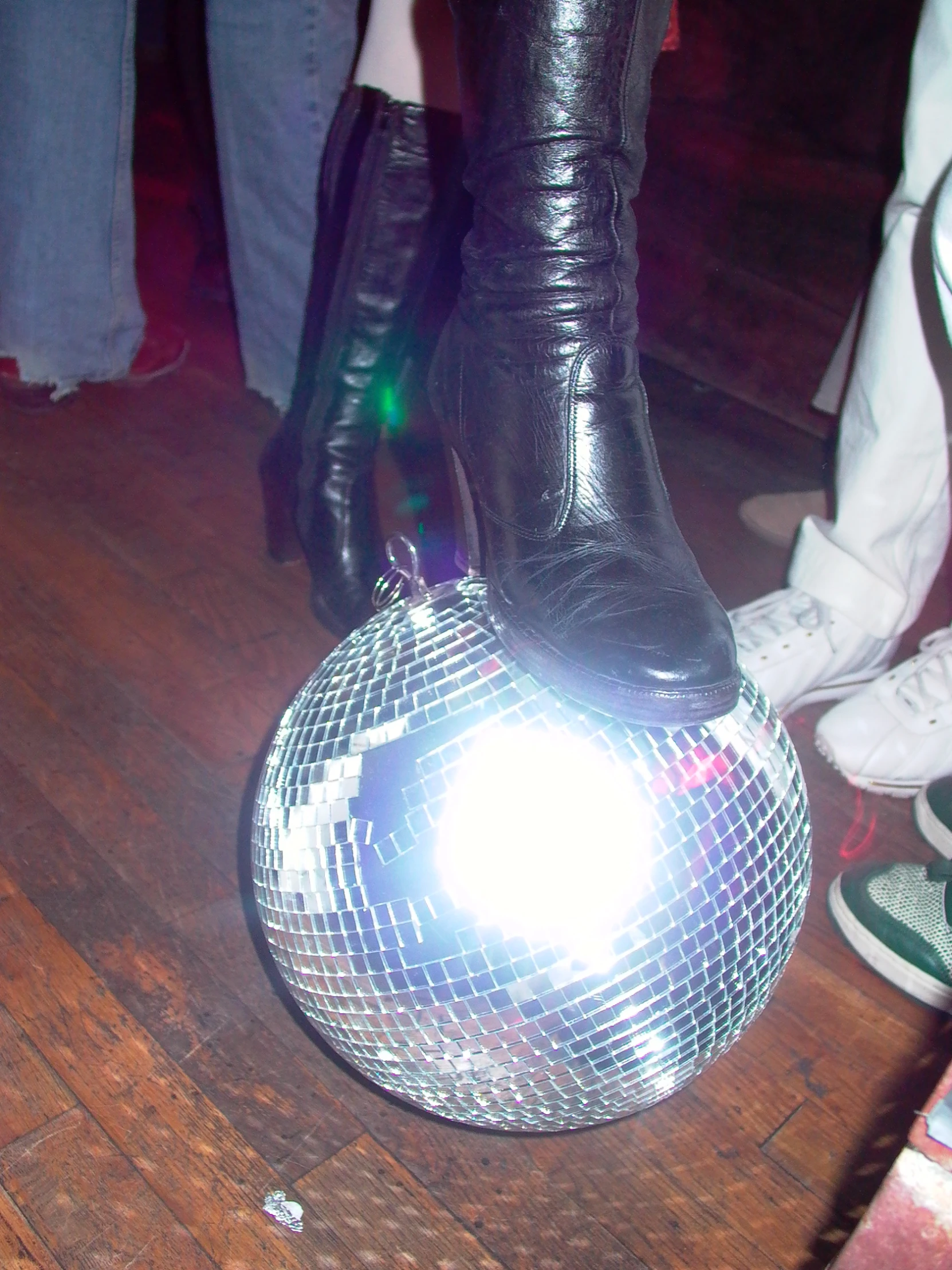 disco ball on wooden floor near foot wearing boots