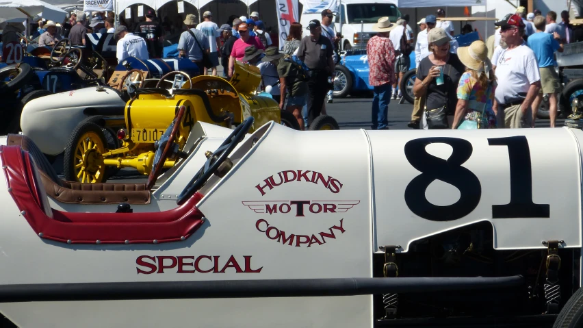 many people are in an outdoor market with antique cars