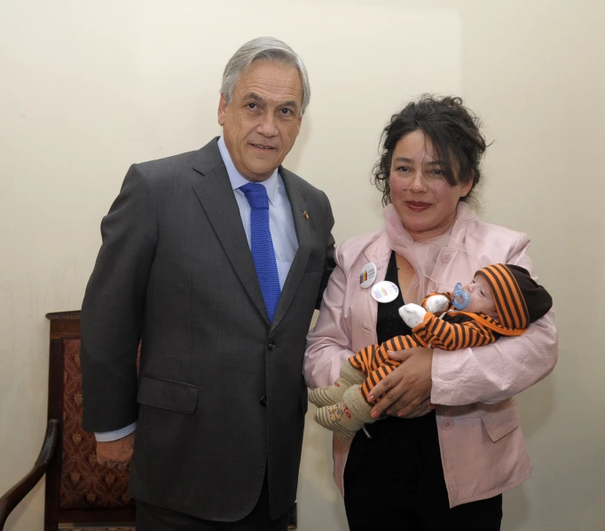 a man in suit and tie standing next to a woman holding a baby