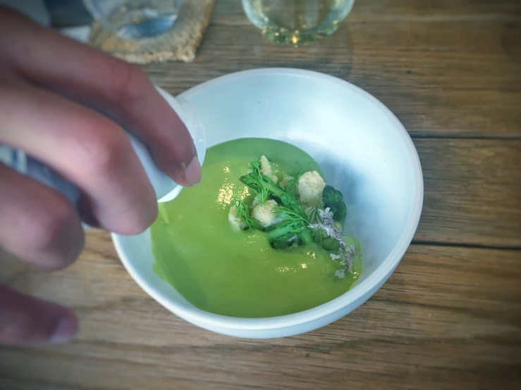 a small bowl with broccoli in it being eaten by a hand