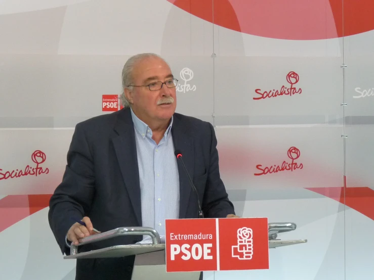 a man is speaking at a podium with a sign behind him