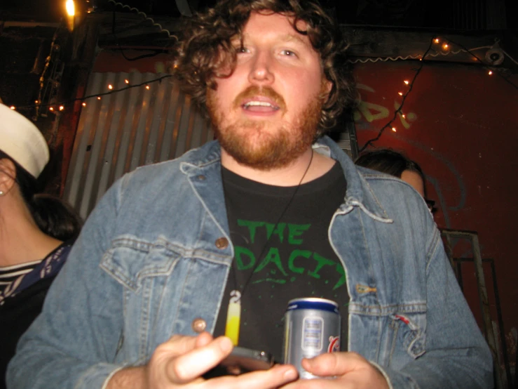 a man holding a can of beer in one hand and looking at his phone