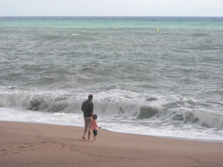 a man and a child standing on top of a sandy beach