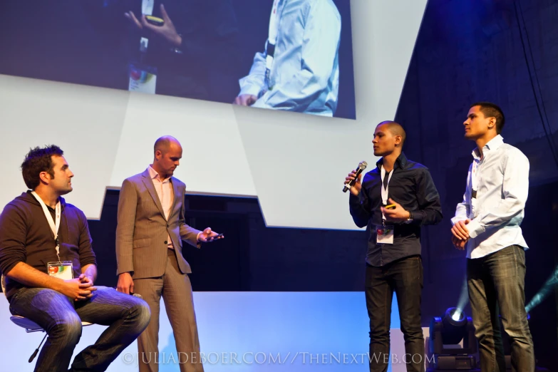 three men standing on stage speaking to each other