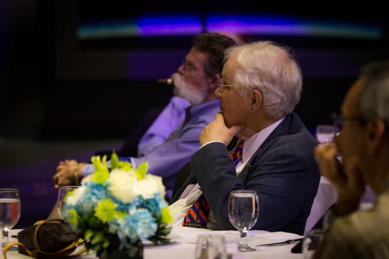 three people sitting at a table, and one is staring at the other man