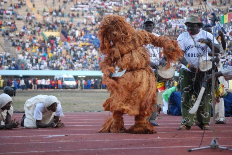 a man in costume stands at the end of a track with drummers