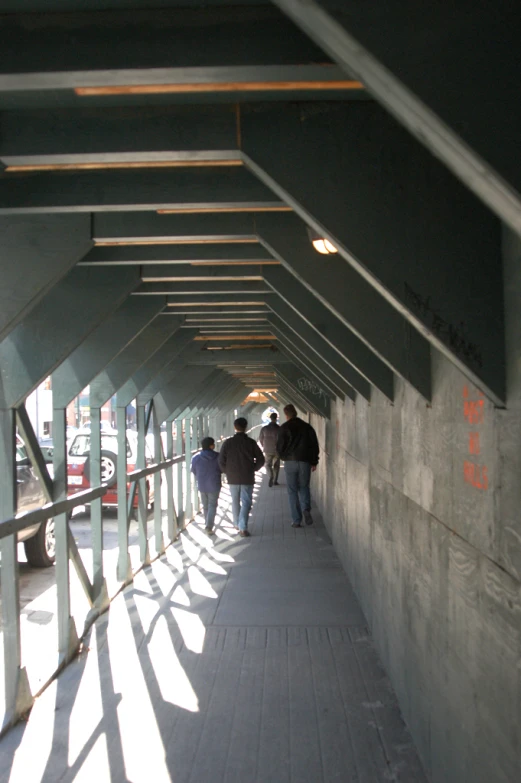 several people walking along the walkway with cars parked in the distance