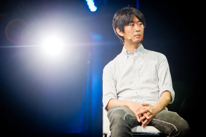 a young asian male sits in a chair with his legs crossed on his knees