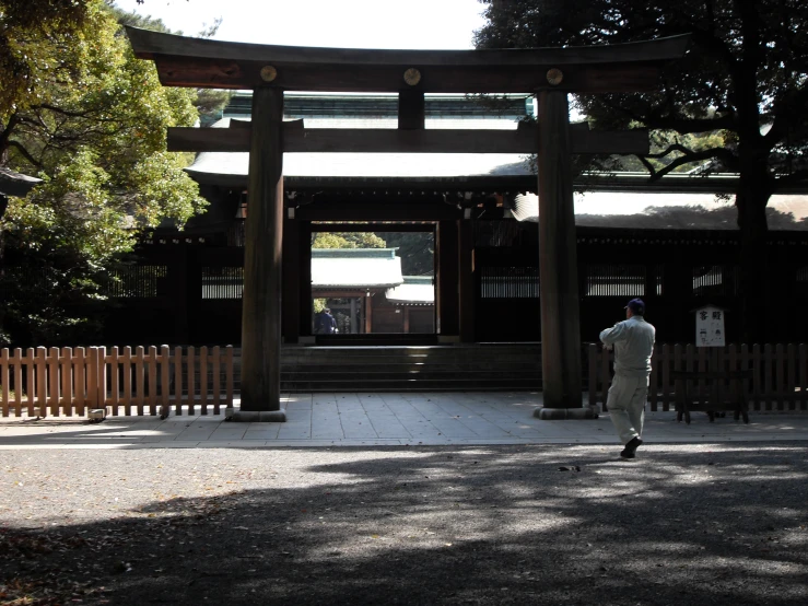 man wearing gray pants walking past a structure with a bell