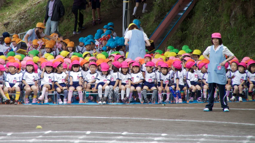 a group of children with large colored hats in front of a crowd