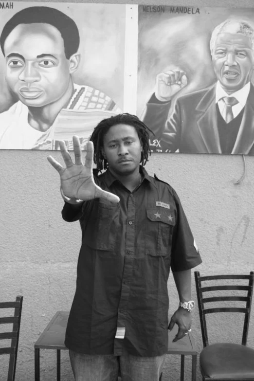 a man in a blue shirt is giving the v sign while a painting of martin luther king is on a wall behind him