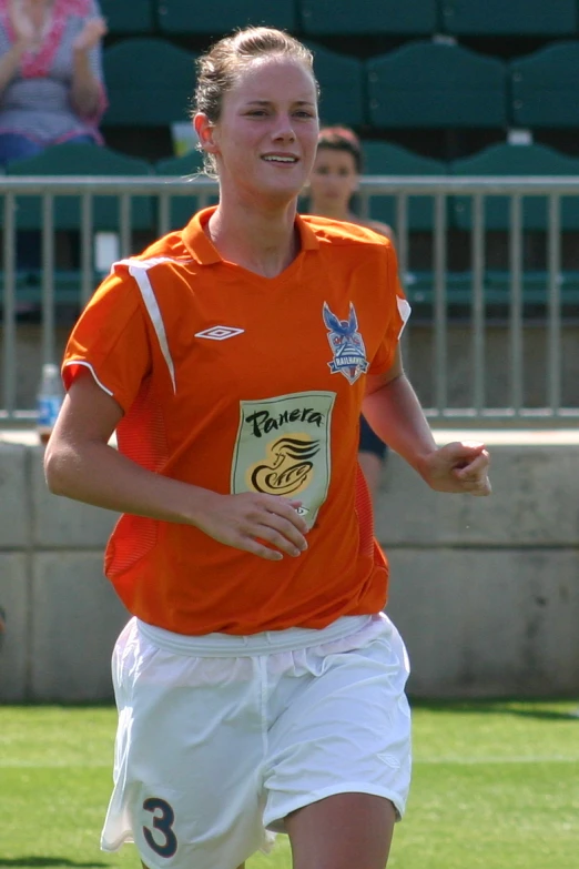 a girl in orange shirt and white shorts playing soccer